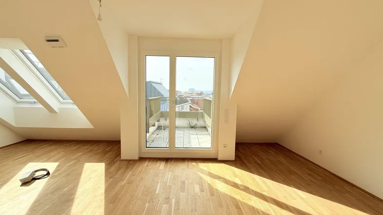 Helles Dachgeschosszimmer mit Parkettboden, Dachfenstern und Zugang zu einer Terrasse.
