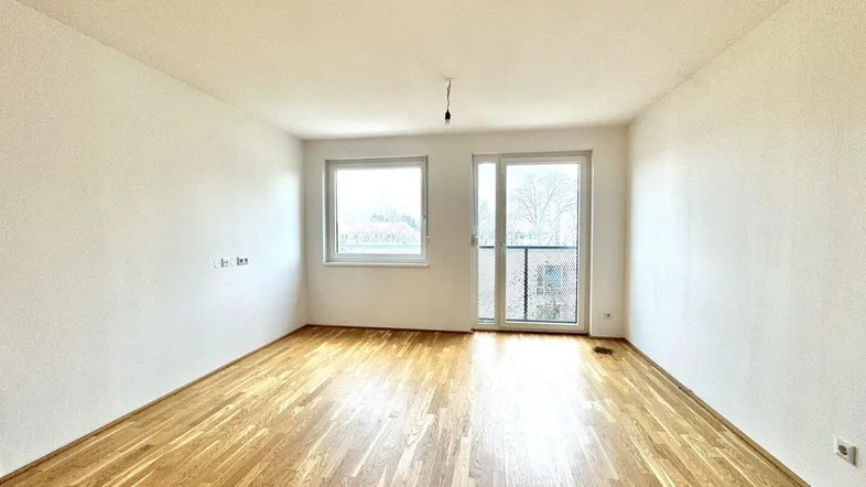 Helles, leeres Zimmer mit Parkettboden und Zugang zu einem französischen Balkon.