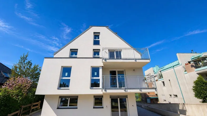 Ansicht der modernen weißen Fassade eines Neubaus mit mehreren Balkonen und klaren Linien.