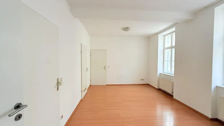 Helles, leeres Zimmer mit Laminatboden und weißen Wänden, bereit zur individuellen Gestaltung.