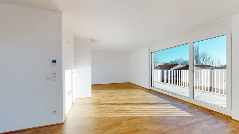 Helles, leeres Wohnzimmer mit Parkettboden und Zugang zu einer großen Terrasse.
