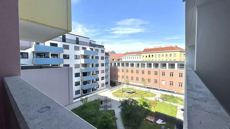 Blick von der Loggia auf den begrünten Innenhof mit Spielbereich und umliegenden modernen Gebäuden.