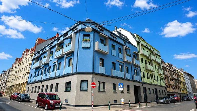 Buntes Eckgebäude mit modernen Fassaden in Blau und Grün an einer städtischen Straße.