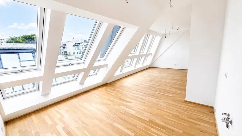 Heller Dachgeschossraum mit Holzboden und großen Dachfenstern, die viel Tageslicht hereinlassen.