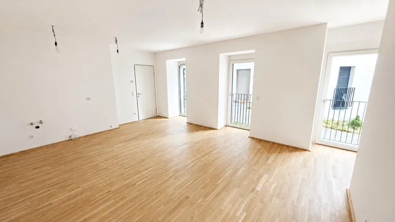 Helles, leeres Zimmer mit Parkettboden und Zugang zu mehreren französischen Balkonen.