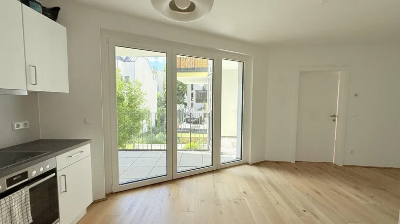 Helles offenes Wohnzimmer mit integrierter Küche, Parkettboden und Zugang zum Balkon.