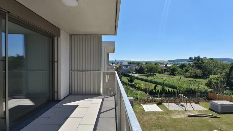 Geräumiger Balkon mit Fliesenboden, Metallgeländer und weitem Blick über die grüne Landschaft.