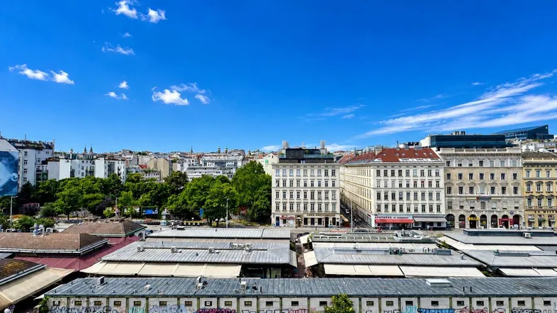 Panoramablick über die Stadt mit historischen Gebäuden, Marktständen und Bahngleisen unter blauem Himmel.