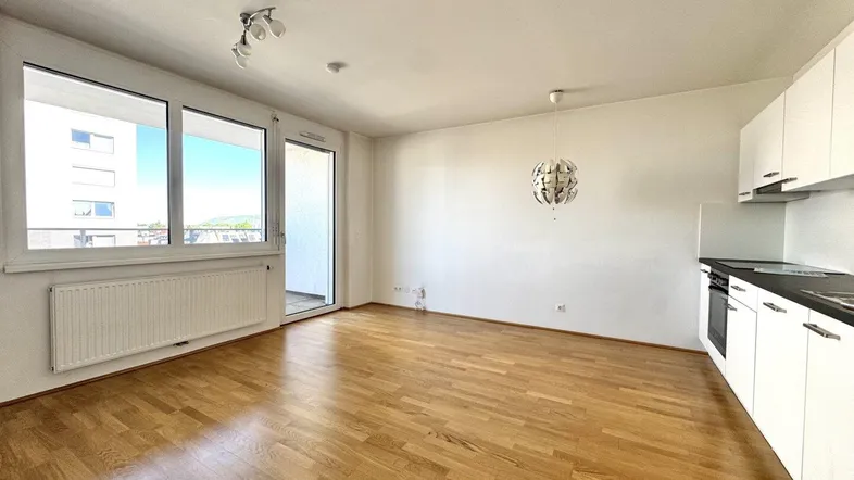 Helles Wohnzimmer mit integrierter Küchenzeile, Parkettboden und Zugang zum Balkon.