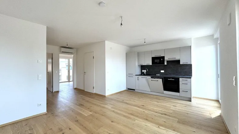Heller offener Wohn-Essbereich mit moderner Einbauküche und Parkettboden, ideal für geselliges Beisammensein.