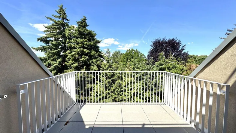 Heller Balkon mit Fliesenboden und weißem Geländer, umgeben von grünen Bäumen unter blauem Himmel.