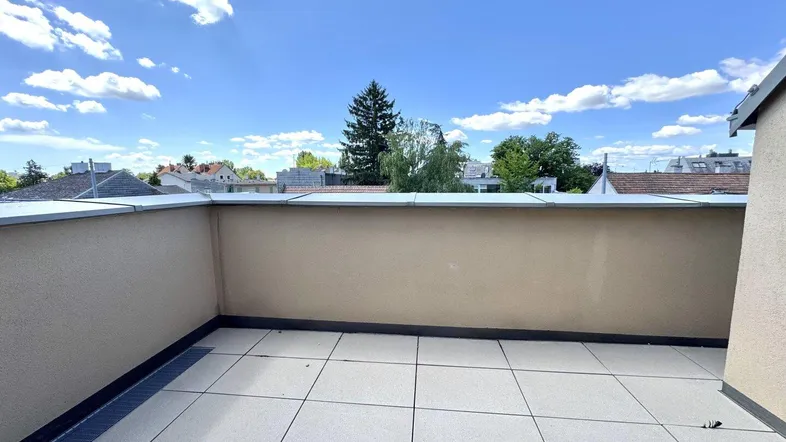 Geräumige Dachterrasse mit Fliesenboden und weitem Blick über die Umgebung unter blauem Himmel.