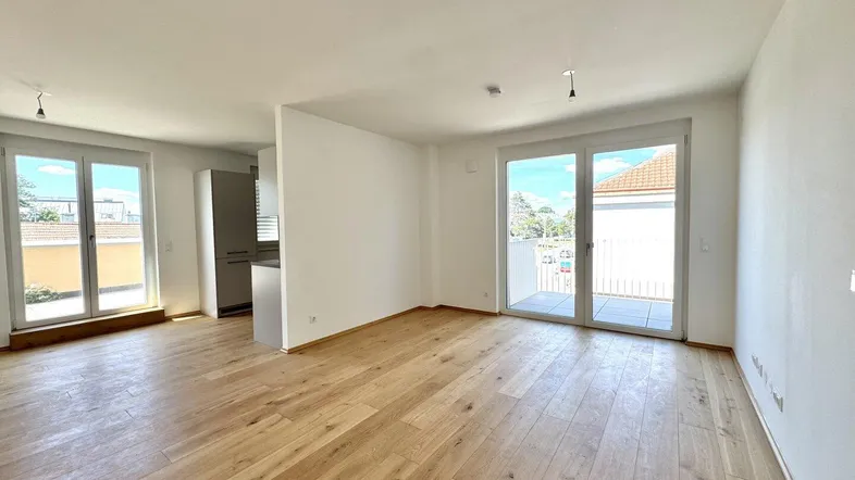 Heller offener Wohnbereich mit Holzboden und Zugang zu einem Balkon oder einer Terrasse.