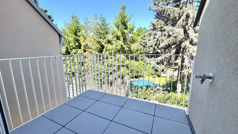 Heller Balkon mit modernen Fliesen und Blick ins Grüne mit einem Gemeinschaftspool.