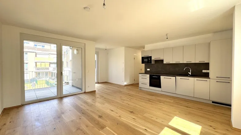 Helles Wohnzimmer mit offener Küche, Holzboden und Zugang zu einem geräumigen Balkon.