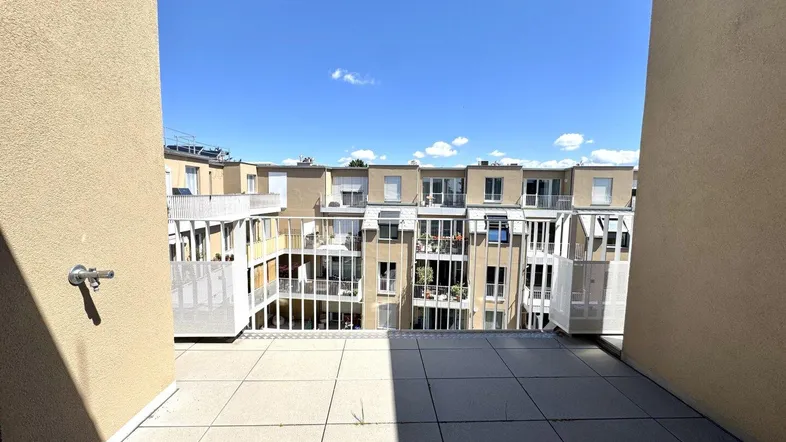 Geräumiger Balkon mit Fliesenboden und Blick auf die umliegenden Gebäude und den Innenhof.