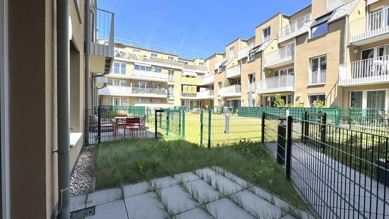 Außenbereich einer modernen Wohnanlage mit gepflasterter Terrasse und kleinem Gartenbereich.