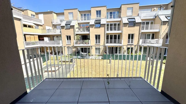 Blick vom Balkon auf den Innenhof mit weiteren Wohngebäuden und Grünflächen.