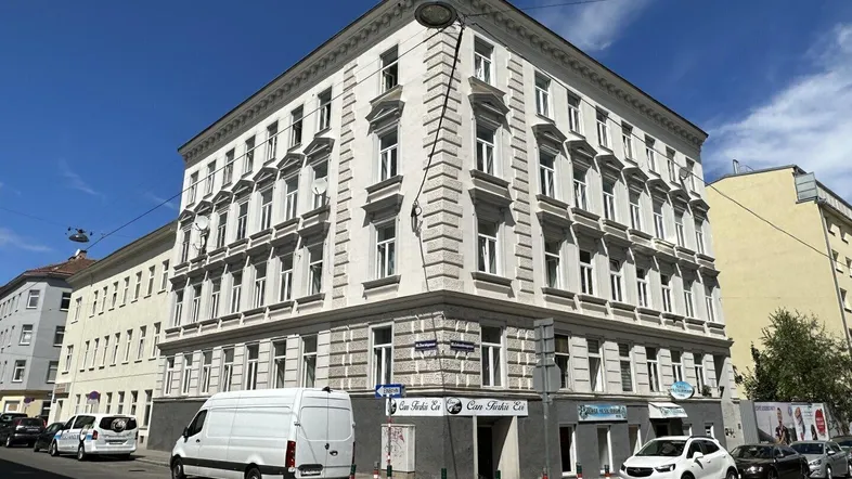 Eckgebäude mit klassischer Fassade und Geschäften im Erdgeschoss in städtischer Umgebung.
