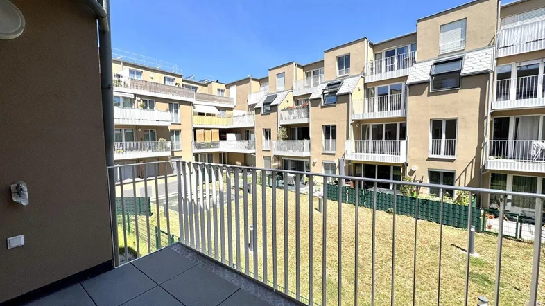 Blick von einem Balkon auf den begrünten Innenhof einer modernen Wohnanlage mit weiteren Balkonen.