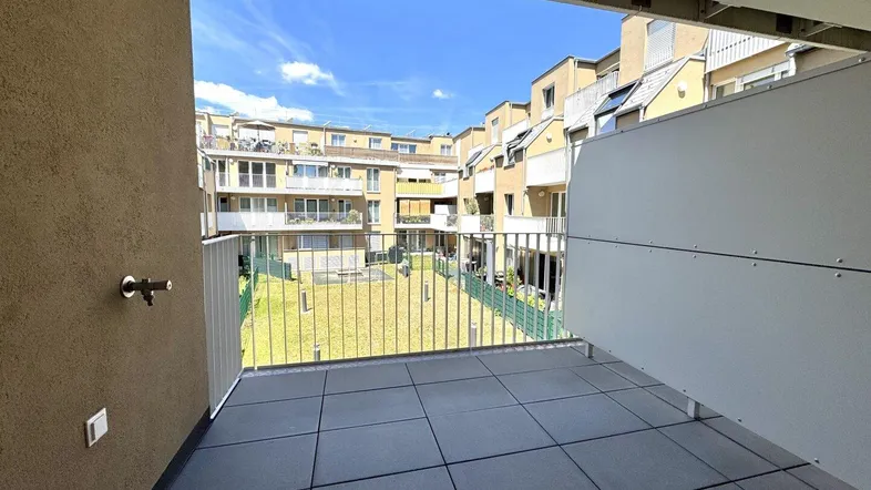 Geräumiger Balkon mit Blick auf den begrünten Innenhof und die umliegenden Wohngebäude.
