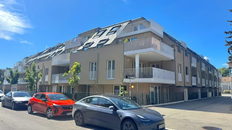 Modernes Mehrfamilienhaus mit mehreren Balkonen und Dachschrägen unter blauem Himmel.