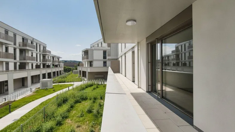 Langer Balkon mit Blick auf die umliegenden Neubauten und grüne Flächen unter blauem Himmel.