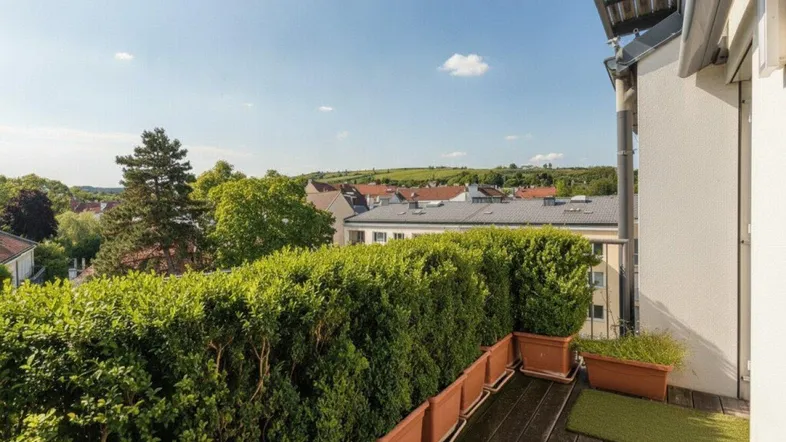 Balkon mit Holzboden, grünen Hecken und weitem Blick über die Dächer der Stadt.