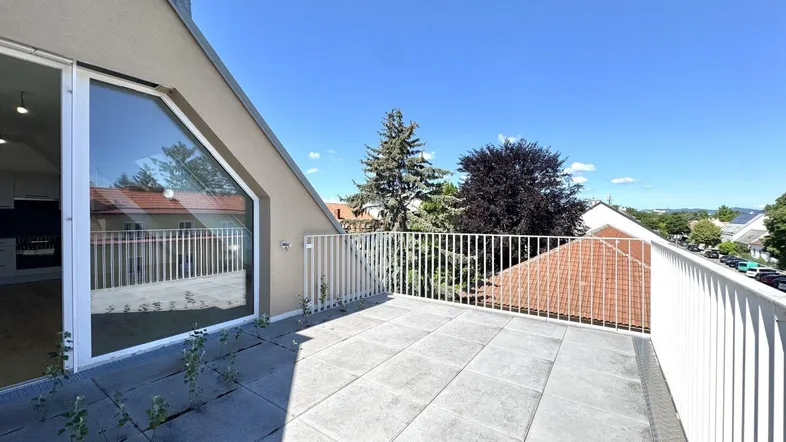 Geräumige Dachterrasse mit Fliesenboden und Blick auf die Umgebung unter blauem Himmel.
