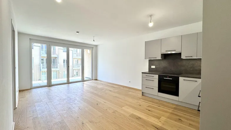 Heller offener Wohnbereich mit integrierter Küchenzeile und Zugang zum Balkon.