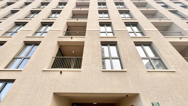 Blick von unten auf die moderne Fassade eines Mehrfamilienhauses mit zahlreichen Balkonen und Fenstern.
