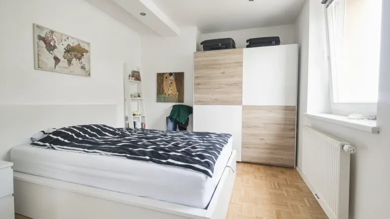 Helles Schlafzimmer mit Parkettboden, großem Kleiderschrank und Fenster für natürliches Licht.