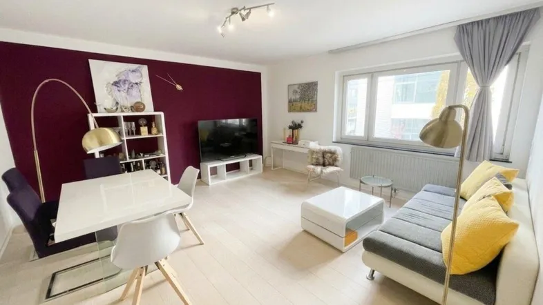 Helles Wohn- und Esszimmer mit moderner Einrichtung, Holzboden und einer Akzentwand in Burgunderrot.