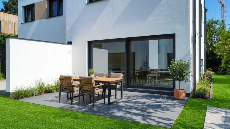 Moderne Terrasse mit Gartenmöbeln und direktem Zugang zum Haus, umgeben von Grünflächen.