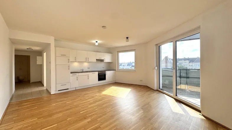 Helles Wohnzimmer mit integrierter Küche, Parkettboden und Zugang zum Balkon.