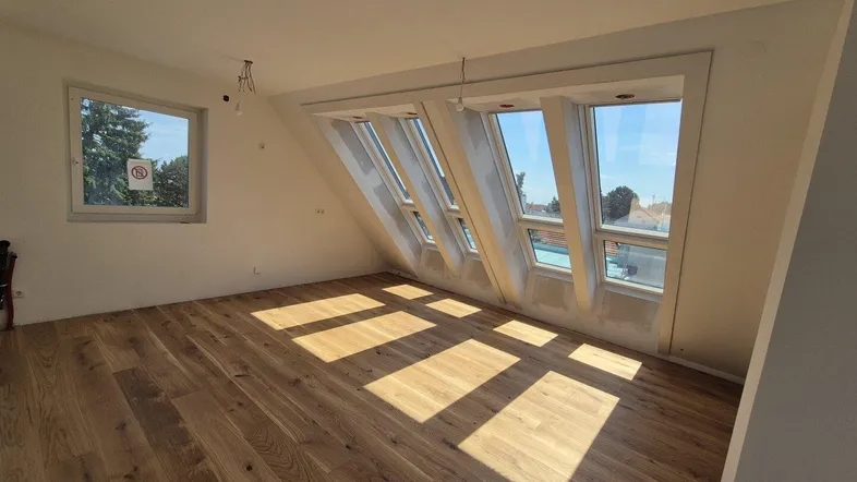 Helles Dachgeschosszimmer mit Holzboden und mehreren Dachfenstern, die viel Tageslicht hereinlassen.