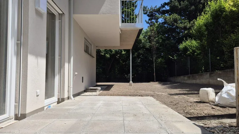 Außenbereich mit gepflasterter Terrasse, ungestaltetem Gartenbereich und Balkon im Obergeschoss.