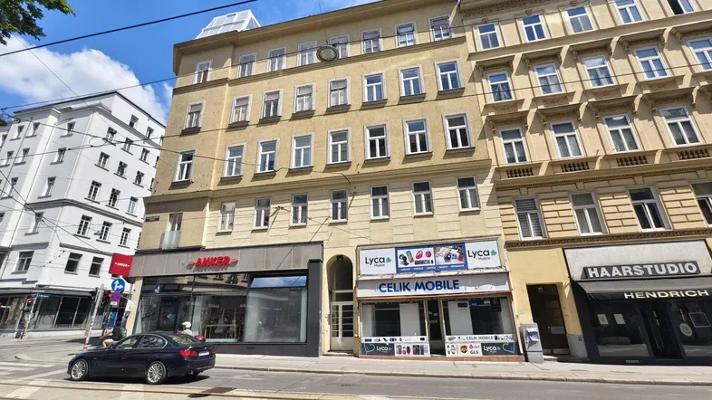 Mehrstöckiges Gebäude mit Geschäften im Erdgeschoss und Wohnungen darüber an einer belebten Straße.
