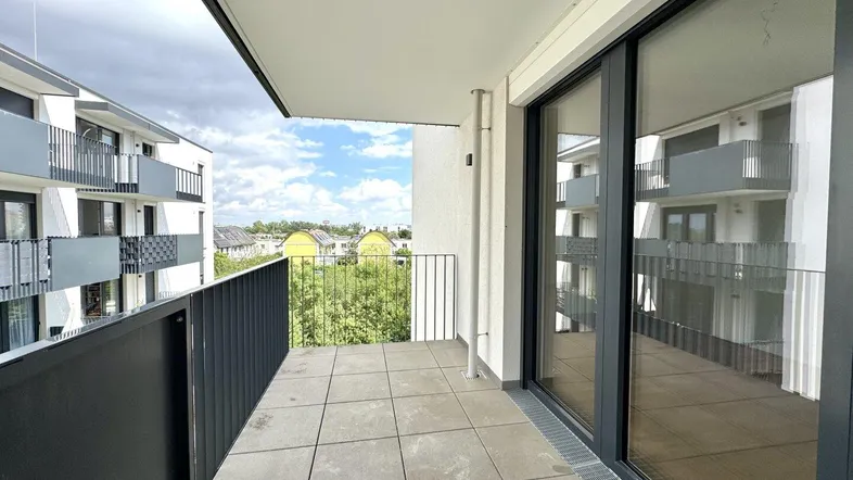 Geräumiger Balkon mit Fliesenboden und Blick auf die umliegenden modernen Gebäude und Grünflächen.