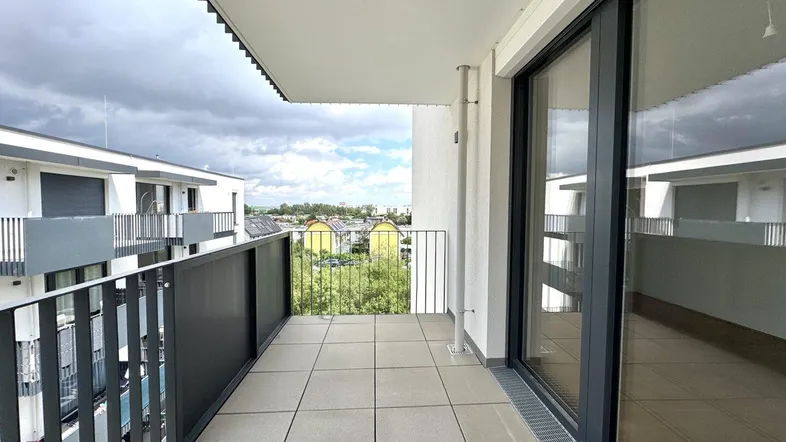 Geräumiger Balkon mit Fliesenboden und Blick auf die umliegenden Gebäude und Grünflächen.