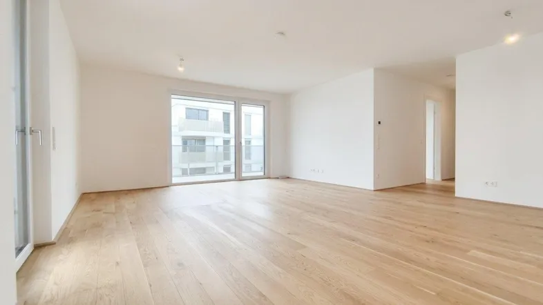 Geräumiges Wohnzimmer mit hellem Parkettboden und Blick auf die umliegenden Gebäude.
