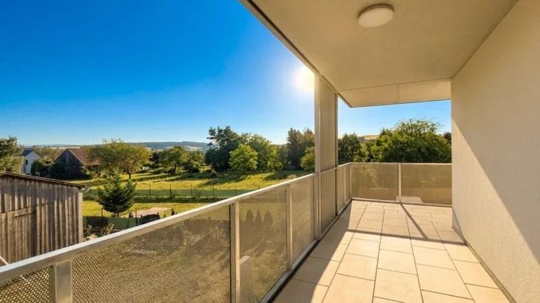 Sonniger Balkon mit Fliesenboden und weitem Blick über die grüne Landschaft.