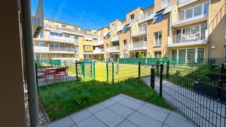 Gepflegter Innenhof mit Rasenfläche und gepflasterter Terrasse, umgeben von modernen Wohngebäuden.
