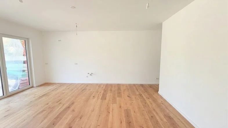 Heller, leerer Raum mit Holzboden und großen Fenstern, bereit für die individuelle Einrichtung.