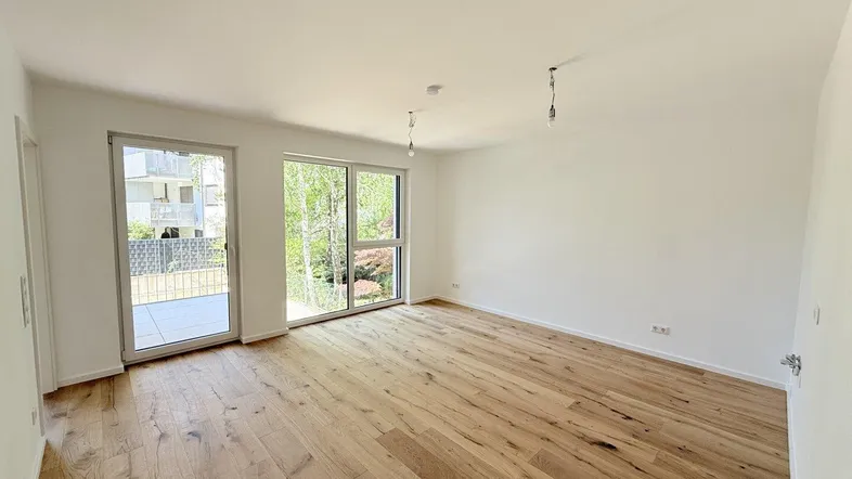 Helles, leeres Zimmer mit Holzboden und Zugang zu einem Balkon, ideal als Wohnbereich.