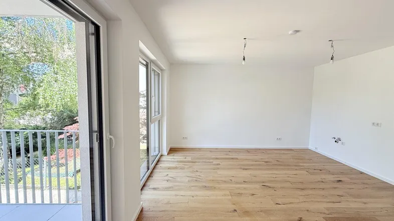 Helles, leeres Wohnzimmer mit neuem Holzboden und Zugang zu einem Balkon.