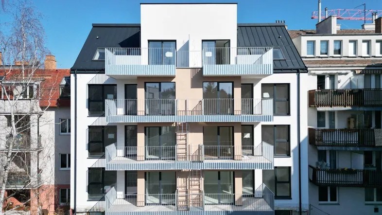 Moderne Fassade eines Neubaus mit mehreren Balkonen und großen Fenstern in städtischer Umgebung.