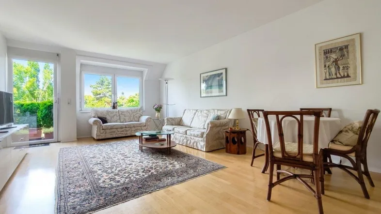 Helles Wohn- und Esszimmer mit Parkettboden, Teppich und Zugang zu einem Balkon.