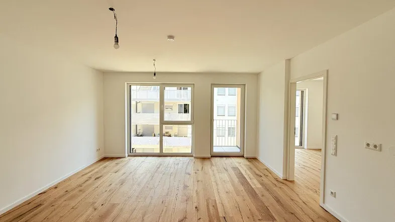 Helles, leeres Wohnzimmer mit neuem Holzboden und großen Fenstern, die viel Tageslicht hereinlassen.