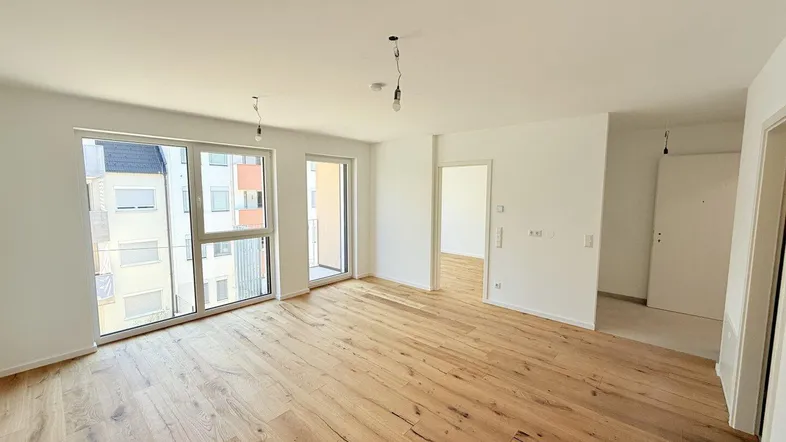 Helles, leeres Wohnzimmer mit neuem Holzboden und großen Fenstern, die viel Tageslicht hereinlassen.